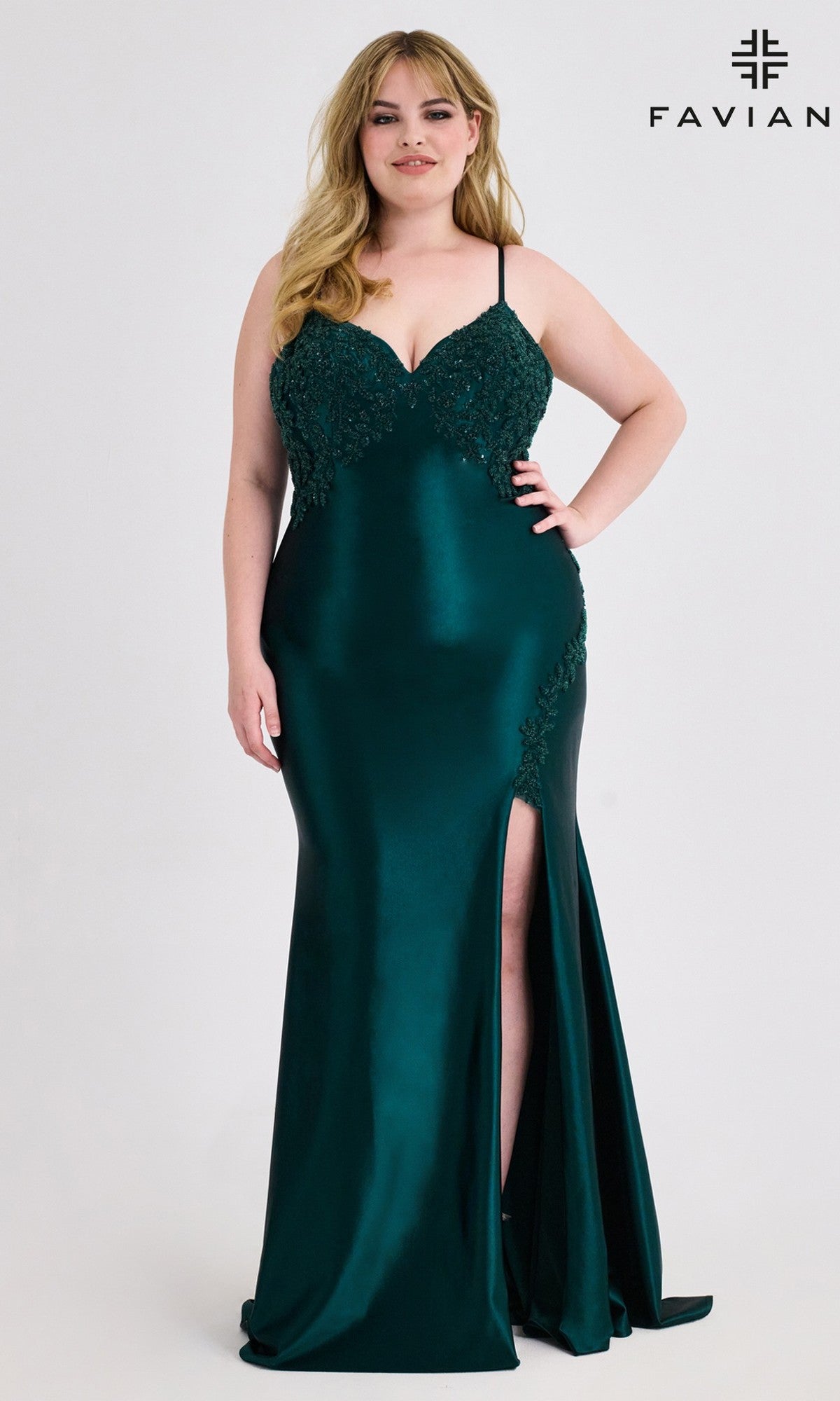 A woman stands before a plain background wearing the Faviana 9597 plus-size beaded-corset prom gown in dark hunter green, featuring thin straps, a fitted silhouette, lace detailing, and a thigh-high slit.